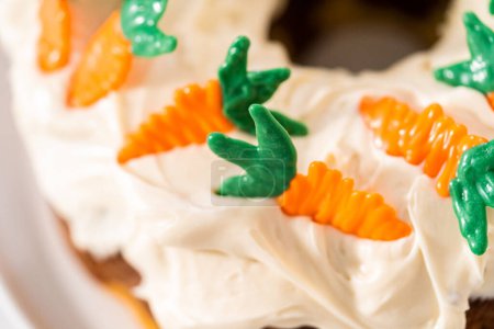 Photo for Decorating freshly baked carrot bundt cake with cream cheese frosting with chocolate carrot cake toppers. - Royalty Free Image