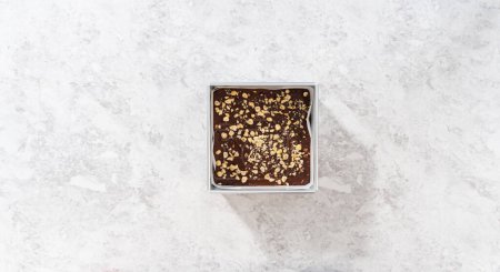 Photo for Flat lay. Filling square cheesecake pan lined with parchment paper with fudge mixture to prepare chocolate hazelnut fudge. - Royalty Free Image