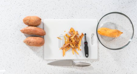 Téléchargez les photos : Pose plate. Peler les patates douces avec un éplucheur de pommes de terre pour faire des patates douces rôties au four - en image libre de droit