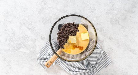 Photo for Flat lay. Melting chocolate chips and other ingredients in a glass mixing bowl over boiling water to prepare chocolate hazelnut fudge. - Royalty Free Image