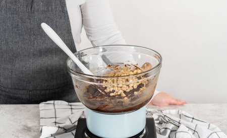 Foto de Derretir chispas de chocolate blanco y otros ingredientes en un tazón de vidrio sobre agua hirviendo para preparar chocolate macadamia fudge. - Imagen libre de derechos
