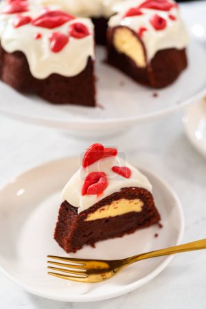 Photo for Slicing freshly baked red velvet bundt cake with chocolate lips and hearts over cream cheese glaze for Valentines Day. - Royalty Free Image