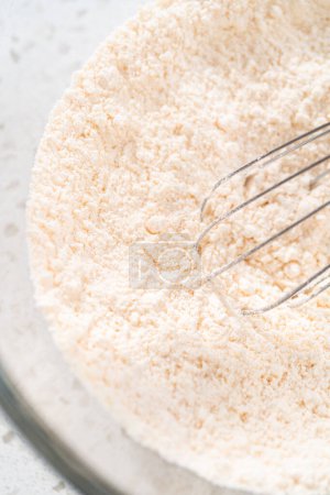 Téléchargez les photos : Mélanger les ingrédients secs avec un fouet à la main dans un grand bol de mélange en verre pour faire cuire un gâteau bundt vanille simple. - en image libre de droit