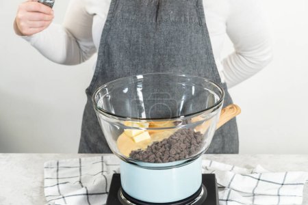 Téléchargez les photos : Fondre les pépites de chocolat blanc et d'autres ingrédients dans un bol de mélange en verre sur de l'eau bouillante pour préparer le caramel à la canne à sucre. - en image libre de droit