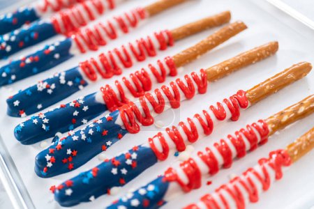 Photo for Homemade chocolate-covered pretzel rods decorated like the American flag drying on a baking sheet lined with parchment paper. - Royalty Free Image