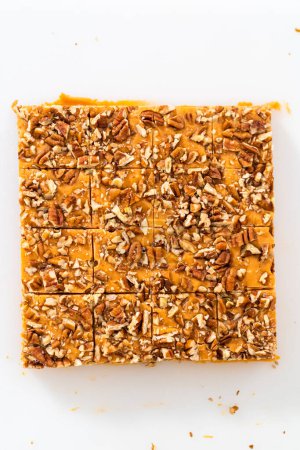 Téléchargez les photos : Couper le caramel à la citrouille en morceaux carrés sur une planche à découper blanche. - en image libre de droit