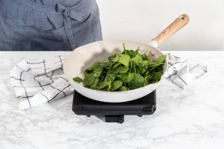 Téléchargez les photos : Frying fresh spinach in a nonestick frying pan to prepare garlic shrimp pasta with spinach. - en image libre de droit