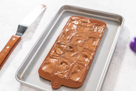 Téléchargez les photos : Remplissage de moule en silicone au chocolat noir fondu pour préparer des mini chocolats gourmands avec des saupoudres. - en image libre de droit