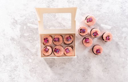 Foto de Acostado. Embalaje recién horneado cupcakes de chocolate fresa adornado con mini chocolates gourmet rosa en una caja de cupcakes de papel blanco. - Imagen libre de derechos