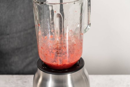 Téléchargez les photos : Mélange de fraises fraîches dans un mélangeur de cuisine pour préparer le glaçage à la crème au beurre aux fraises. - en image libre de droit