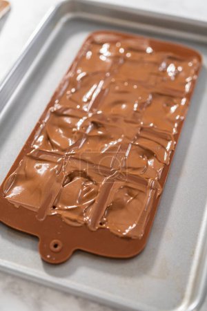 Foto de Rellenar el molde de silicona de chocolate con chocolate negro derretido para preparar mini chocolates gourmet con espolvoreos. - Imagen libre de derechos
