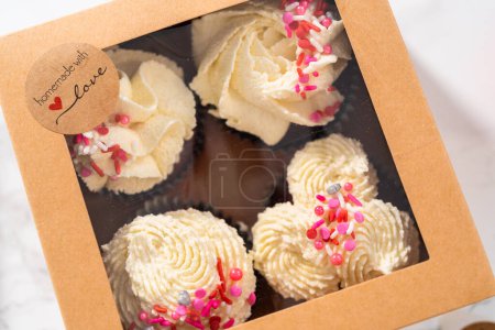 Foto de Envasado de cupcakes de terciopelo rojo recién horneados con glaseado de ganache de chocolate blanco en la caja de cupcakes. - Imagen libre de derechos