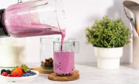 Téléchargez les photos : Pouring freshly made mixed berry boba smoothie into a drinking glass. - en image libre de droit