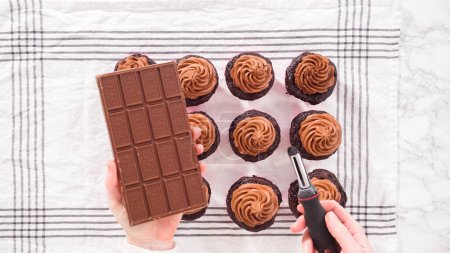 Téléchargez les photos : Pose plate. Pas à pas. Barre de chocolat à raser sur des cupcakes au chocolat givré avec glaçage à la ganache au chocolat. - en image libre de droit