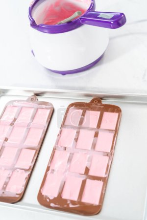 Foto de Llenado de molde de chocolate de silicona con chocolate derretido para hacer mini chocolates rosados. - Imagen libre de derechos