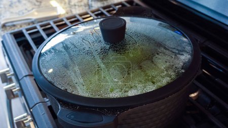 Foto de En una cocina blanca moderna, grandes espárragos orgánicos se cocinan al vapor en una olla de cocción considerable. - Imagen libre de derechos
