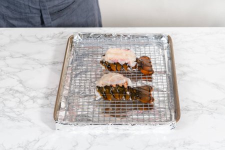 Téléchargez les photos : Queues de homard crues sur une plaque de cuisson avec papier d'aluminium de cuisine, prêtes à être cuites au four. - en image libre de droit