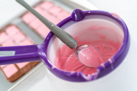 Téléchargez les photos : Remplissage moule de chocolat silicone avec du chocolat fondu pour faire des mini chocolats roses. - en image libre de droit