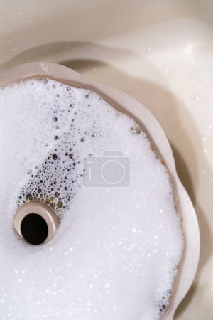 Photo for Soaking dirty aluminum bundt cake pan with soapy water in a kitchen sink. - Royalty Free Image