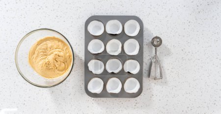 Téléchargez les photos : Pose plate. Scooping pâte cupcake avec cuillère à pâte dans une casserole cupcake cuisson avec doublures pour cuire dulce de leche cupcakes. - en image libre de droit