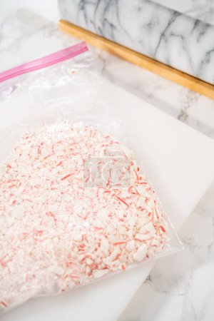 Téléchargez les photos : Broyer des bonbons à la menthe poivrée dans un sac en plastique avec un rouleau en marbre sur une planche à découper blanche. - en image libre de droit
