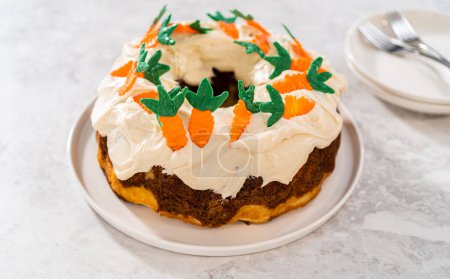 Téléchargez les photos : Trancher le gâteau bundt aux carottes fraîchement cuit avec glaçage au fromage à la crème et garnitures décorées de gâteau aux carottes au chocolat. - en image libre de droit