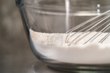 Foto de Mezclar ingredientes secos con un batidor de mano en un tazón de vidrio para hornear magdalenas de semillas de amapola de limón. - Imagen libre de derechos