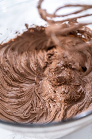 Photo for Mixing store-bought chocolate frosting in a mixing glass bowl with a hand mixer. - Royalty Free Image