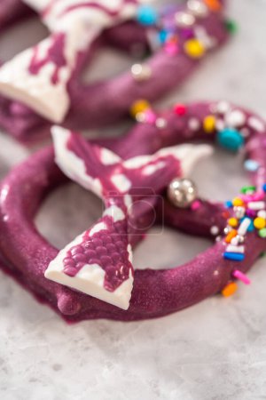 Foto de Homemade chocolate-dipped pretzel twists decorated with colorful sprinkles and chocolate mermaid tails on a white plate. - Imagen libre de derechos