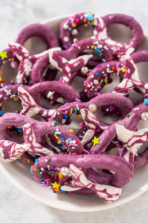 Foto de Homemade chocolate-dipped pretzel twists decorated with colorful sprinkles and chocolate mermaid tails on a white plate. - Imagen libre de derechos