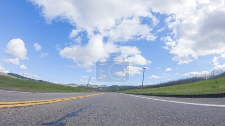 Foto de En un día claro de invierno, un automóvil viaja suavemente a lo largo de la autopista 101 cerca de Santa María, California, bajo un cielo azul brillante, rodeado por una mezcla de vegetación y tonos dorados.. - Imagen libre de derechos