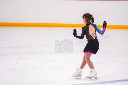 Téléchargez les photos : Petite fille pratiquant avant sa compétition de patinage artistique à la patinoire intérieure. - en image libre de droit