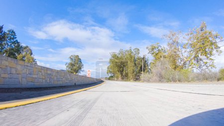Foto de En un día de invierno crujiente, un automóvil cruza a lo largo de la icónica autopista 101 cerca de San Luis Obispo, California. El paisaje circundante es marrón y tenue, con colinas onduladas y parches de costa - Imagen libre de derechos