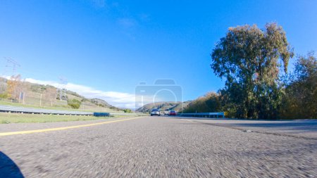 Foto de En un día de invierno crujiente, un automóvil cruza a lo largo de la icónica autopista 1 cerca de San Luis Obispo, California. El paisaje circundante es marrón y tenue, con colinas onduladas y parches de costa - Imagen libre de derechos
