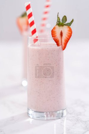 Photo for Freshly made healthy breakfast strawberry banana smoothie garnished with fresh strawberry and paper straw. - Royalty Free Image