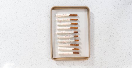 Photo for Flat lay. Homemade candy cane chocolate-covered pretzel rods are drying on a baking sheet lined with parchment paper. - Royalty Free Image