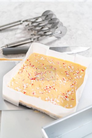 Foto de Extracción de caramelo fudge bastón de una sartén de pastel de queso cuadrado forrado con pergamino. - Imagen libre de derechos