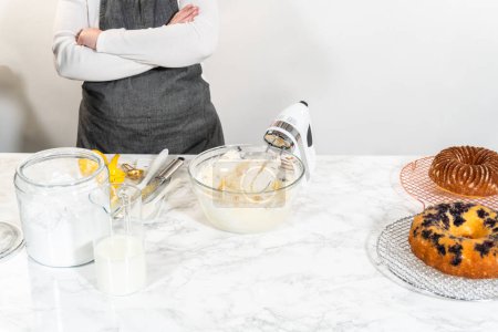 Téléchargez les photos : Combinez habilement les ingrédients à l'aide d'un mélangeur à main pour préparer un glaçage riche et lisse au fromage à la crème au beurre, parfait pour orner le gâteau bundt. - en image libre de droit