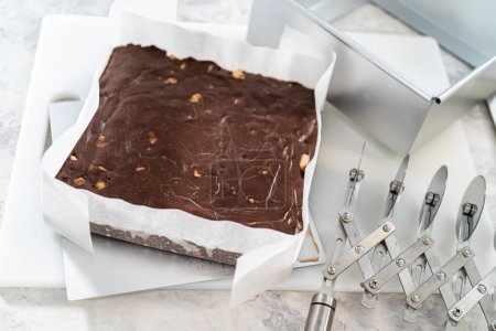 Foto de Extracción de chocolate dulce de macadamia de una sartén cuadrada de pastel de queso forrada con pergamino. - Imagen libre de derechos