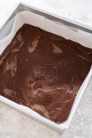 Téléchargez les photos : Remplissage carré moule à gâteau au fromage doublé de papier parchemin avec mélange de caramel pour préparer le caramel à la canne à sucre. - en image libre de droit