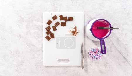 Téléchargez les photos : Pose plate. Arrosant chocolat rose fondu sur le dessus des mini chocolats et saupoudrer quelques saupoudres colorées sur le dessus. - en image libre de droit