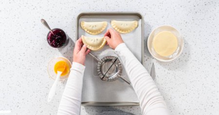 Téléchargez les photos : Pose plate. Remplissage de pâte empanada avec garniture tarte aux myrtilles pour faire des empanadas sucrés aux myrtilles. - en image libre de droit