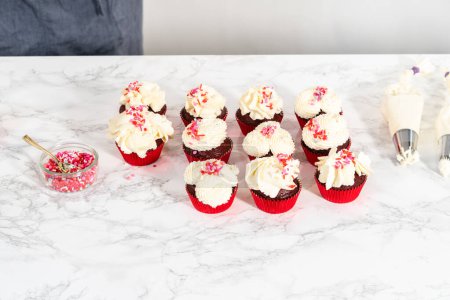 Téléchargez les photos : Piping glaçage ganache chocolat blanc sur le dessus de cupcakes en velours rouge et garniture de saupoudrer. - en image libre de droit