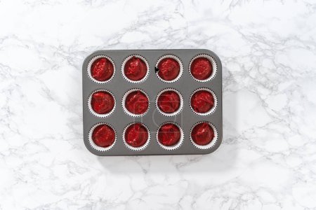 Photo for Flat lay. Scooping cupcake dough with dough scoop into cupcake pan lined with foil liners to bake red velvet cupcakes with white chocolate ganache frosting. - Royalty Free Image