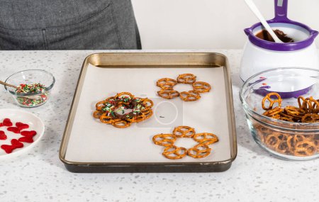 Photo for Dipping pretzels twists into melted chocolate to make a chocolate pretzel Christmas wreath. - Royalty Free Image