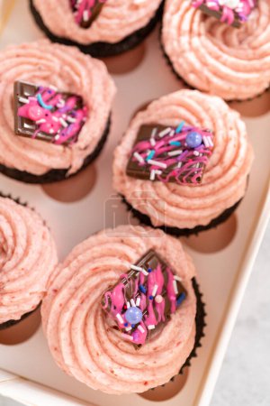 Foto de Embalaje recién horneado cupcakes de chocolate fresa adornado con mini chocolates gourmet rosa en una caja de cupcakes de papel blanco. - Imagen libre de derechos