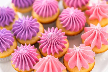 Foto de Mini cupcakes de vainilla recién horneados con glaseado de crema de mantequilla rosa ombre en un soporte de pastel blanco. - Imagen libre de derechos
