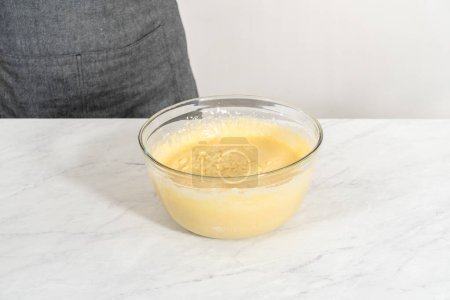 Mélanger les ingrédients dans un grand bol à mélanger en verre pour faire cuire le gâteau bundt aux myrtilles au citron.