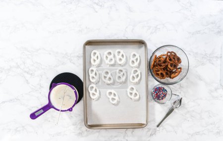 Téléchargez les photos : Flat lay. Dipping pretzels twists into melted chocolate to make red, white, and blue chocolate-covered pretzel twists. - en image libre de droit
