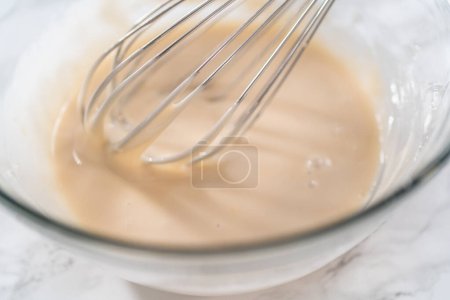 Photo for Lemon glaze. Mixing ingredients with a hand whisk in a glass mixing bowl to make lemon glaze. - Royalty Free Image